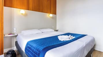 Ein Hotelzimmer mit Bett, Nachttisch, Wandlampe und einer Holzvertäfelung über dem Bett.