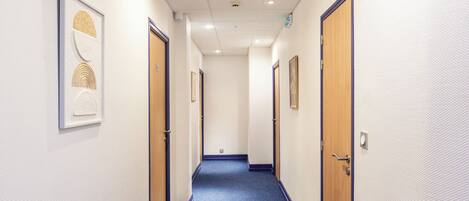A hallway with doors on both sides, a carpeted floor, and framed artwork on the walls.