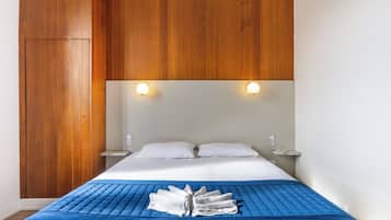 Habitación de hotel con cabecera de madera, dos lámparas de noche, cama con ropa blanca y una almohada decorativa azul.