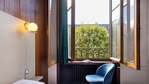 A hotel room with a bed, a desk, a chair, and a window with a view of trees. - Hôtel Bristol Metz Centre Gare (Metz)