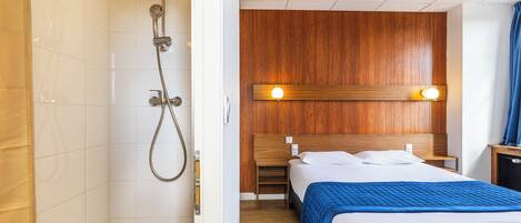 A hotel room with a shower, wooden headboard, and a bed with a blue blanket.