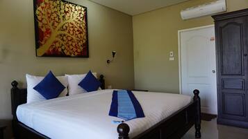 A neatly made bed with blue pillows, a decorative blue and white runner, a large abstract painting on the wall, a dark wooden wardrobe, and a white door.