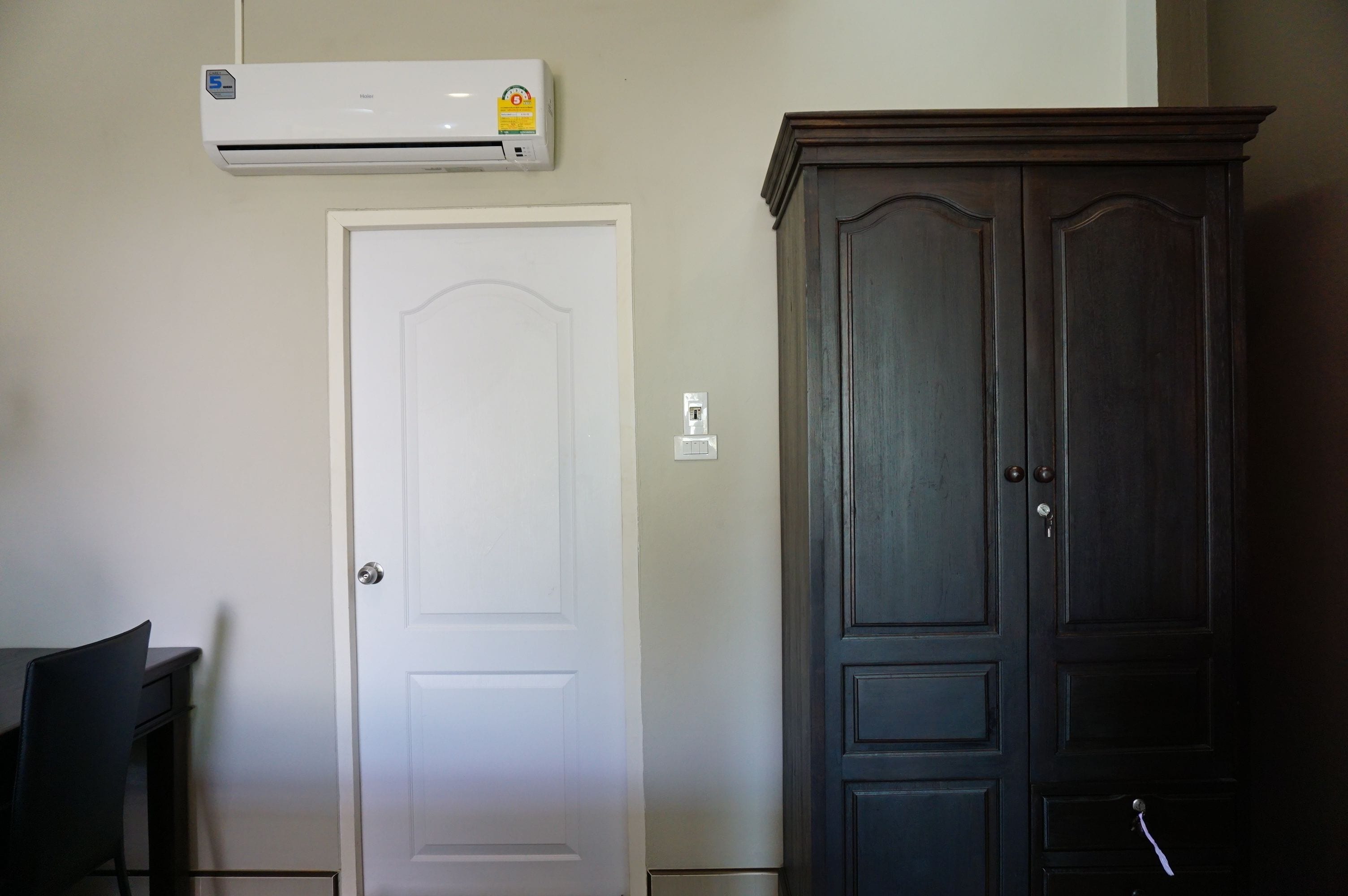 Et værelse med en hvid dør, en mørk træskab og en aircondition installeret på væggen.
