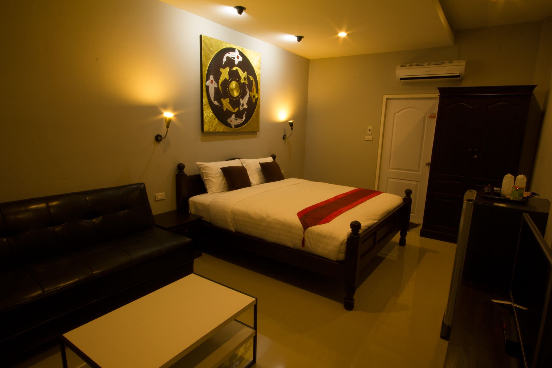 Una habitación de hotel con cama, sofá, una mesita y un equipo de aire acondicionado.