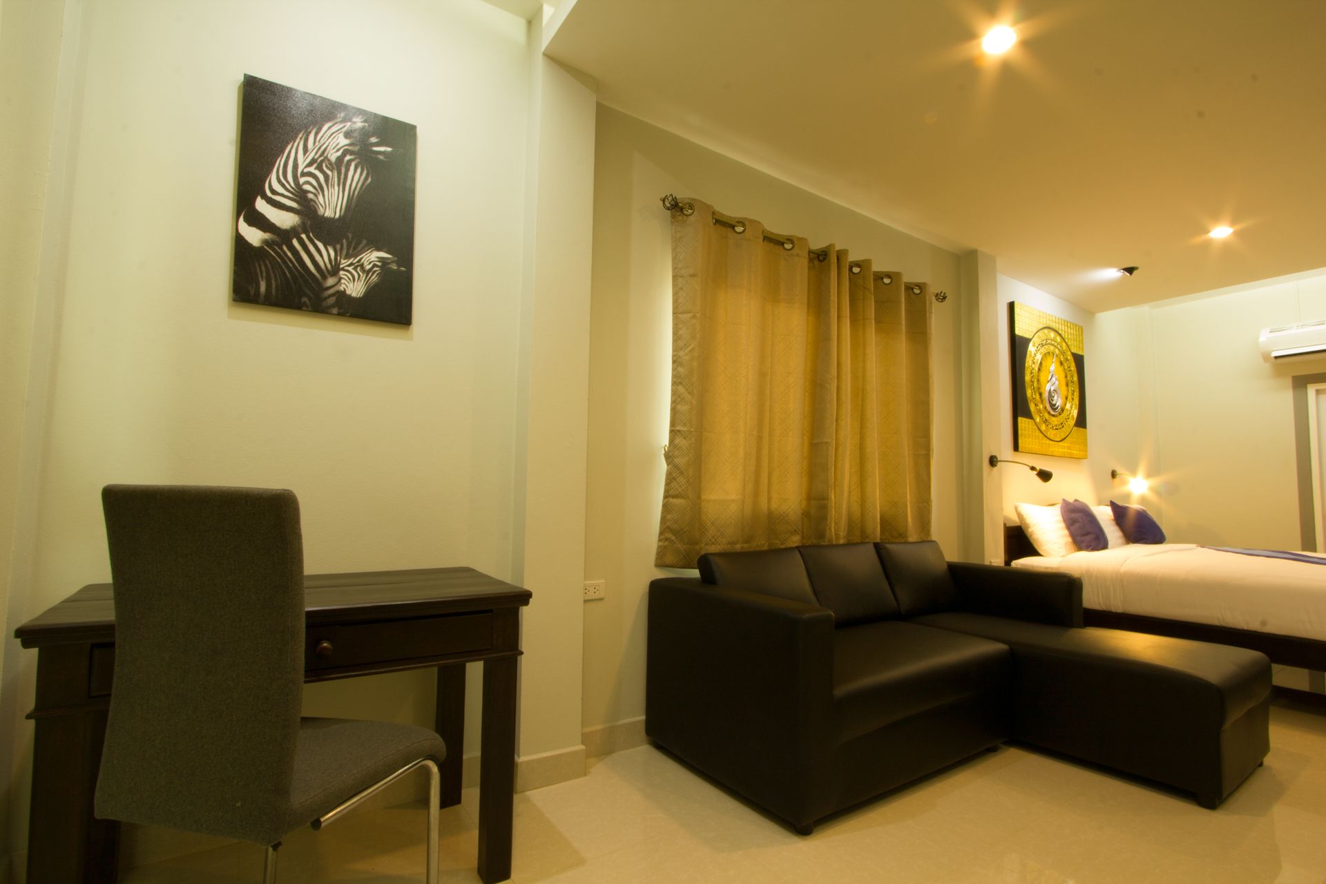 A hotel room with a desk, a sofa, a bed, and a painting on the wall.