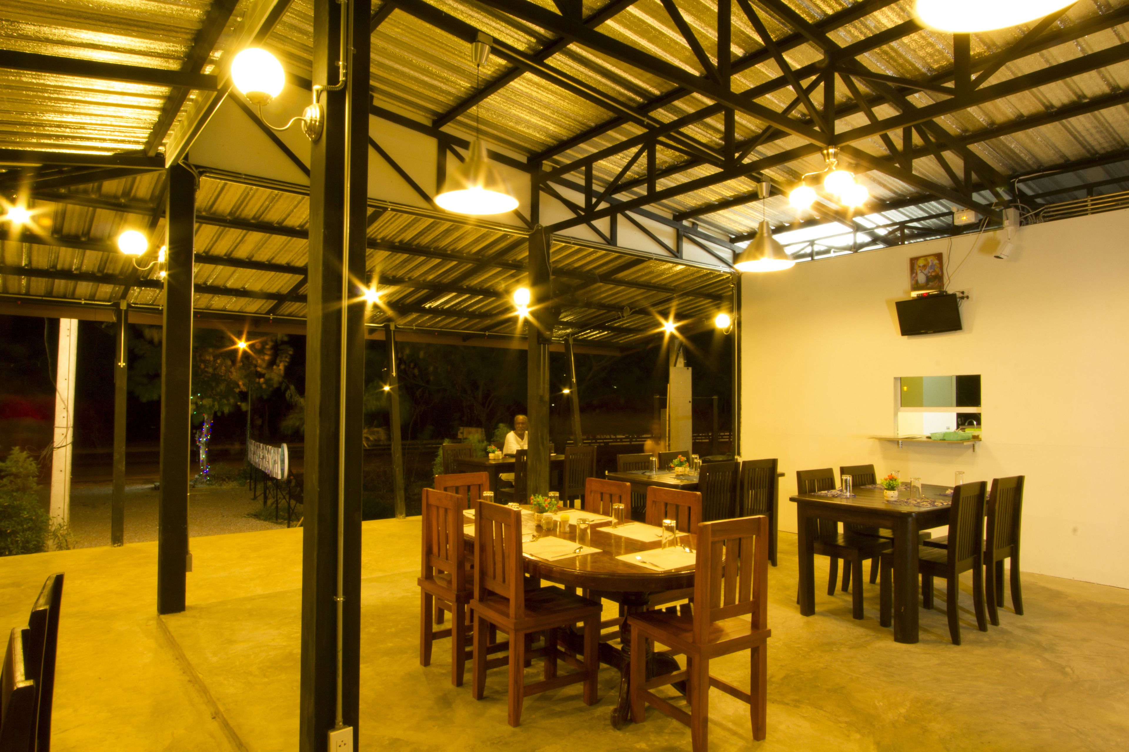 Un comedor interior con mesas y sillas, un techo alto con vigas metálicas e iluminación colgante.