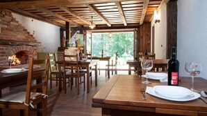 A rustic dining area with wooden tables and chairs, a brick fireplace, and a view of the outdoors. - Plitvica Lodge (Plitvicka Jezera)