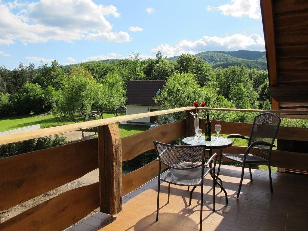 A balcony with a wooden railing, two chairs, a table, and a bottle of wine.