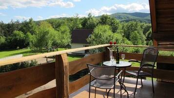 A balcony with a wooden railing, two chairs, a table, and a bottle of wine.