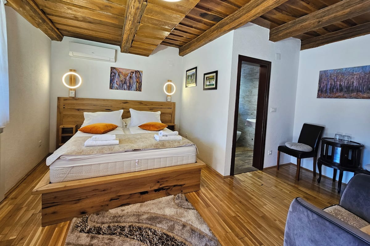 A bedroom with a wooden bed, two bedside lamps, a wooden ceiling, and a stone wall.