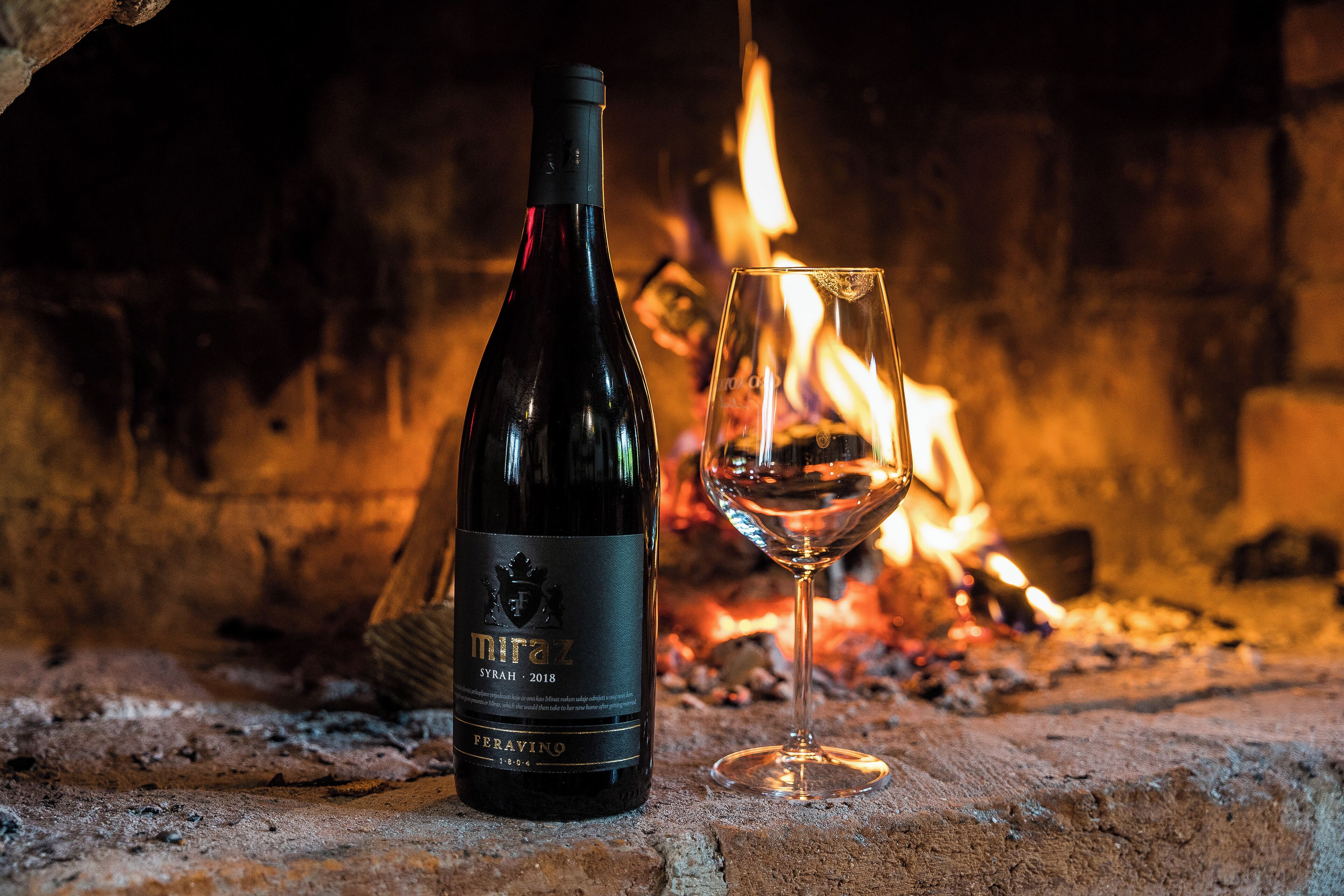 A bottle of Miraz Syrah 2018 wine and a glass of wine in front of a fireplace.