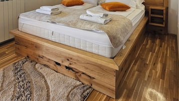 Un lit en bois avec une literie blanche, deux oreillers orange et une petite table de chevet avec une lampe.