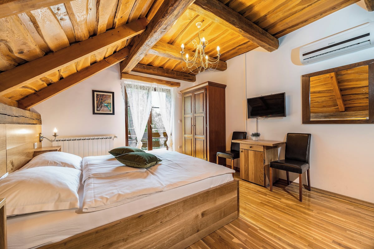 A bedroom with a wooden ceiling, a bed, a desk, a chair, and a TV on the wall.