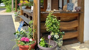 A wooden lodge with a sign reading "Lodge" above the entrance. There are potted plants and a signboard with breakfast and dinner prices. - Plitvica Lodge (Plitvicka Jezera)