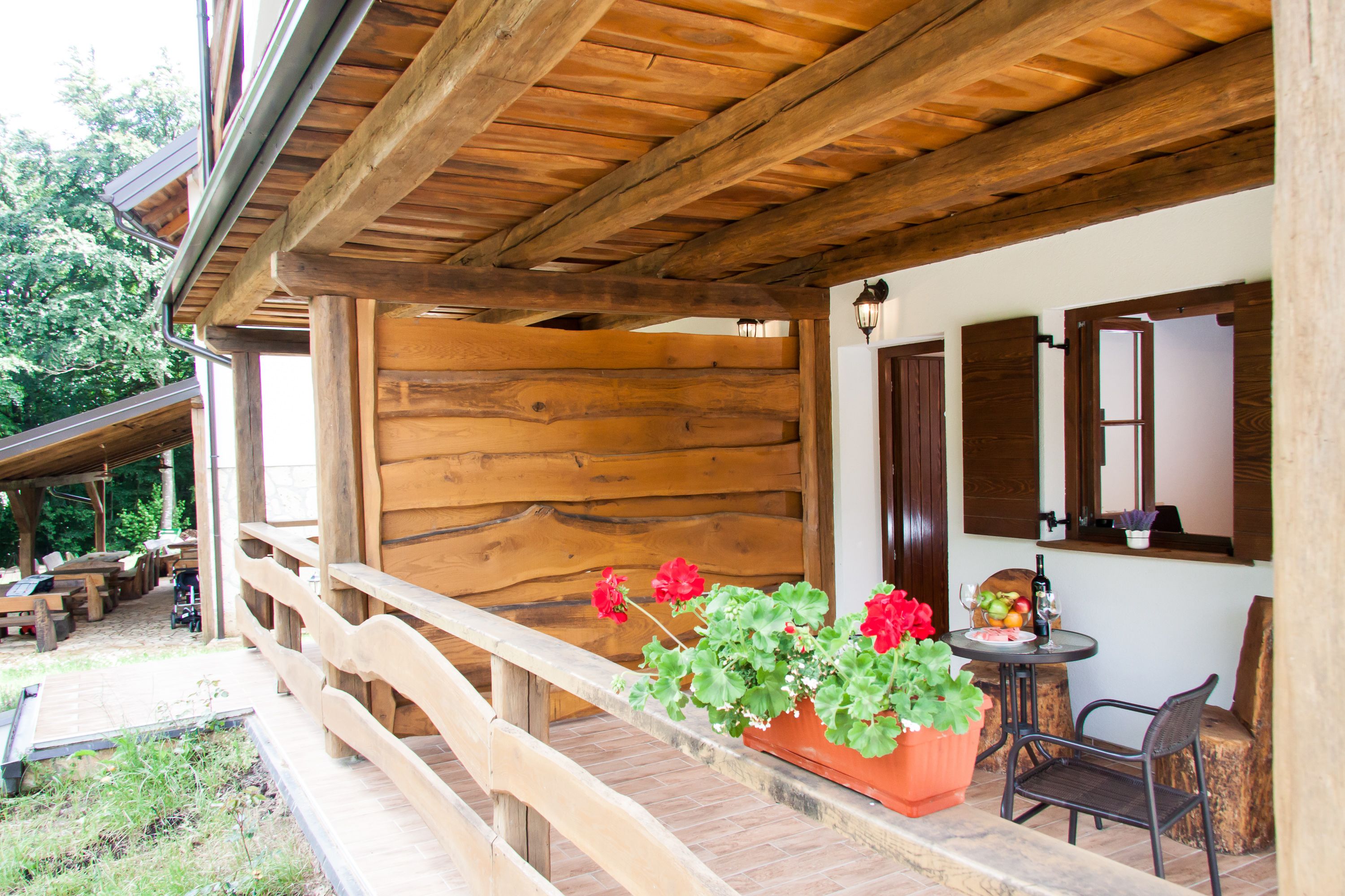 A wooden porch with a wooden railing, a table with chairs, and a potted plant with red flowers.