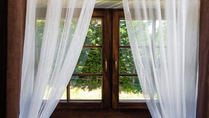 A room with a large window covered by sheer white curtains, offering a view of greenery outside. - Plitvica Lodge (Plitvicka Jezera)