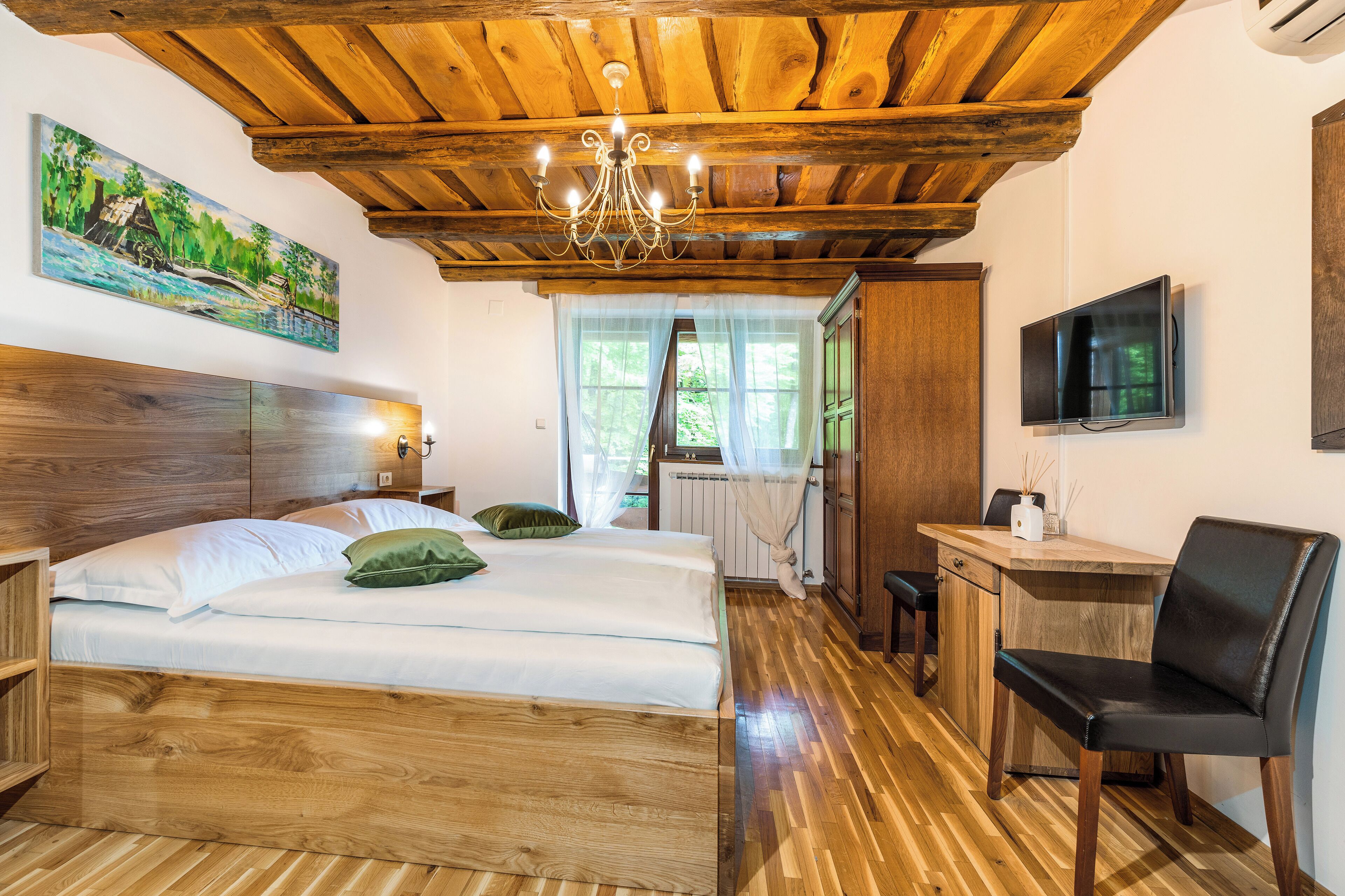 A wooden-floored bedroom with a bed, a desk, and a TV.