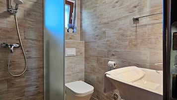 A modern bathroom with a wooden floor, a shower with a glass door, a toilet, and a sink with a towel hanging on it.