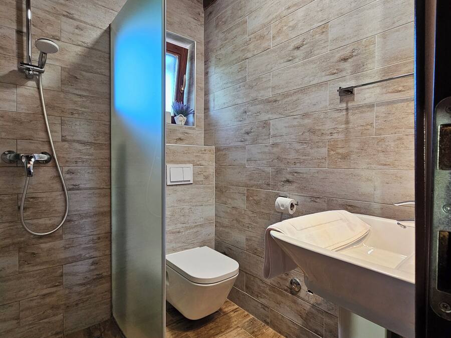 A modern bathroom with a wooden floor, a shower with a glass door, a toilet, and a sink with a towel hanging on it.