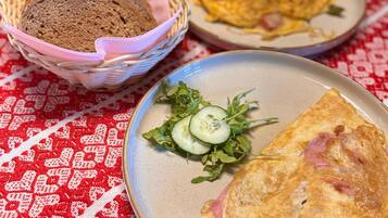 A table with two plates of food, one with an omelette and the other with a salad, and a basket of bread.