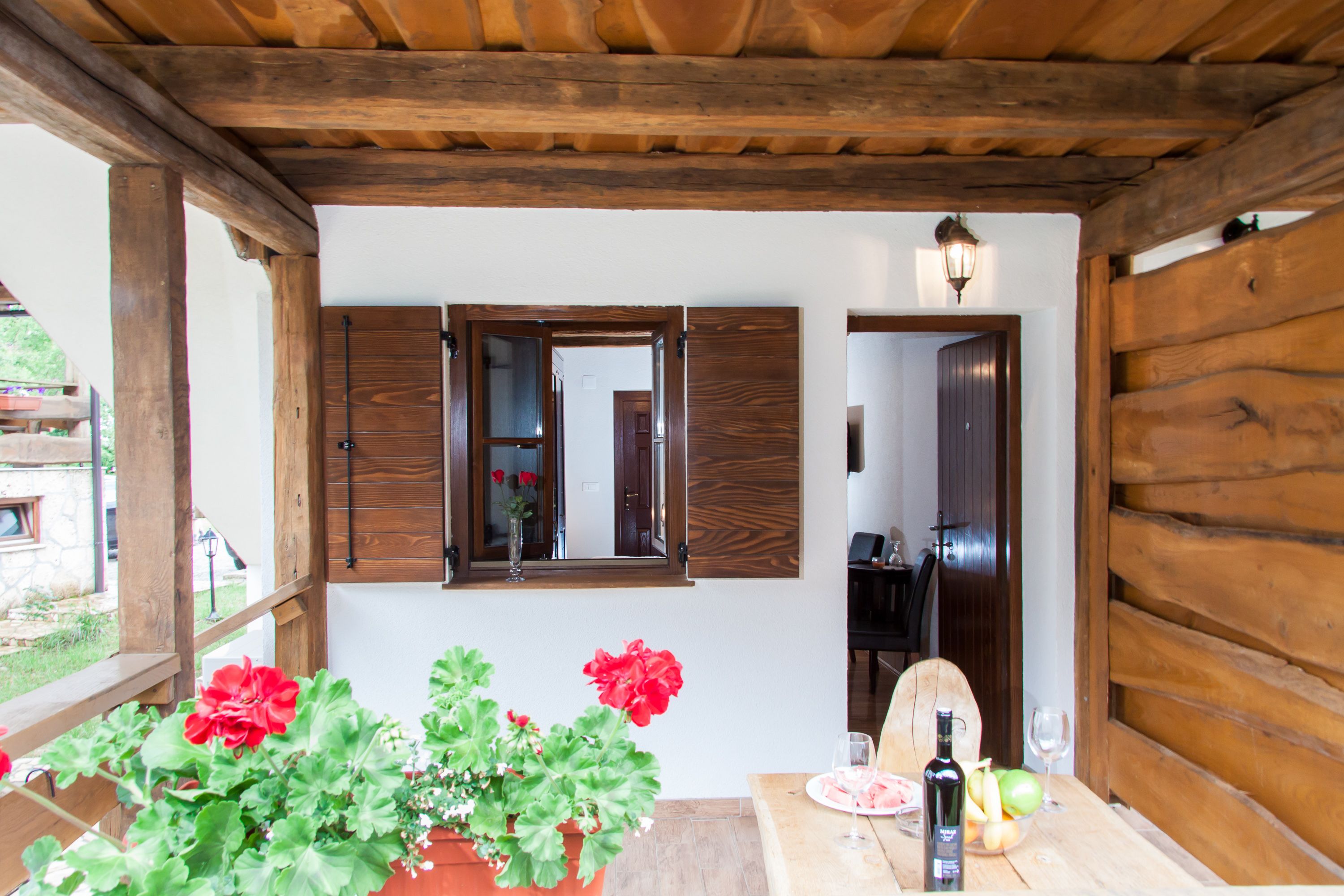 Un patio con estructura de madera, una mesa, plantas en macetas y una botella de aceite de oliva.