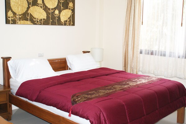Una cama bien hecha con un edredón rojo y una almohada decorativa, una mesita de noche con una lámpara y un cuadro floral grande en la pared.