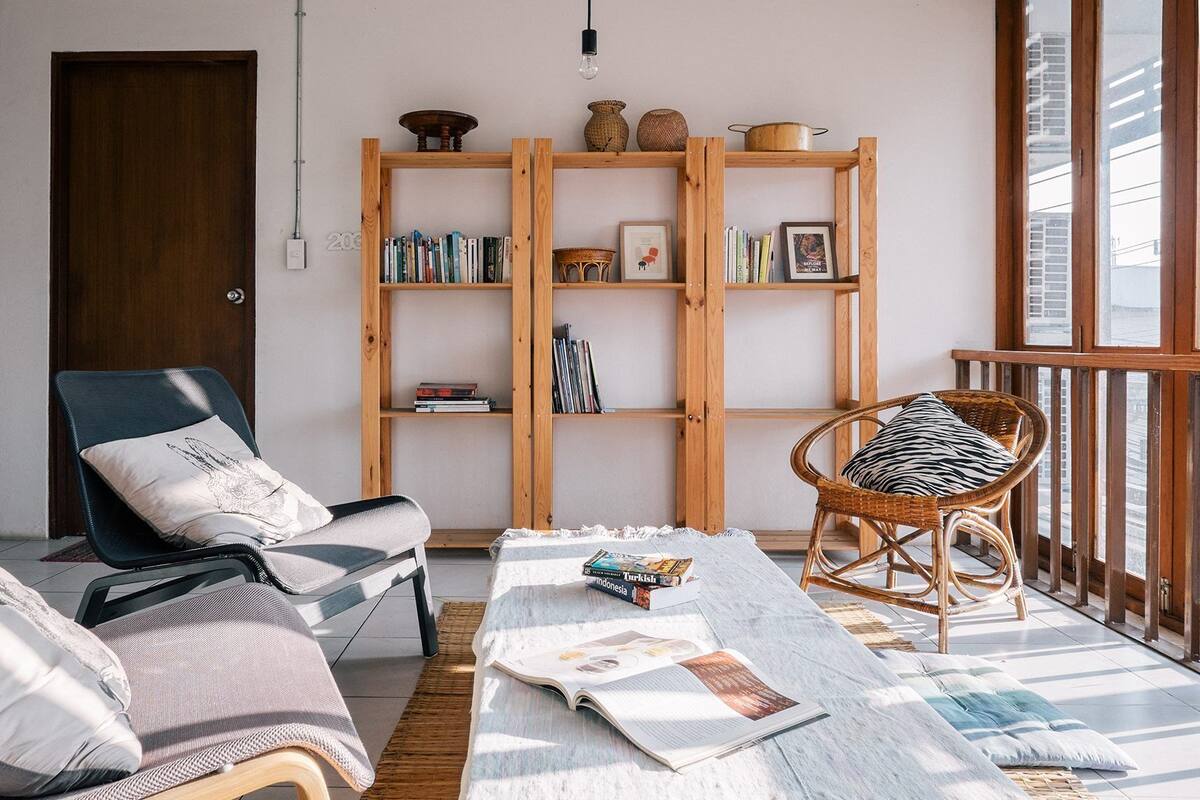 A cozy living room with a wooden bookshelf, a comfortable chair, a sofa, and a large window.