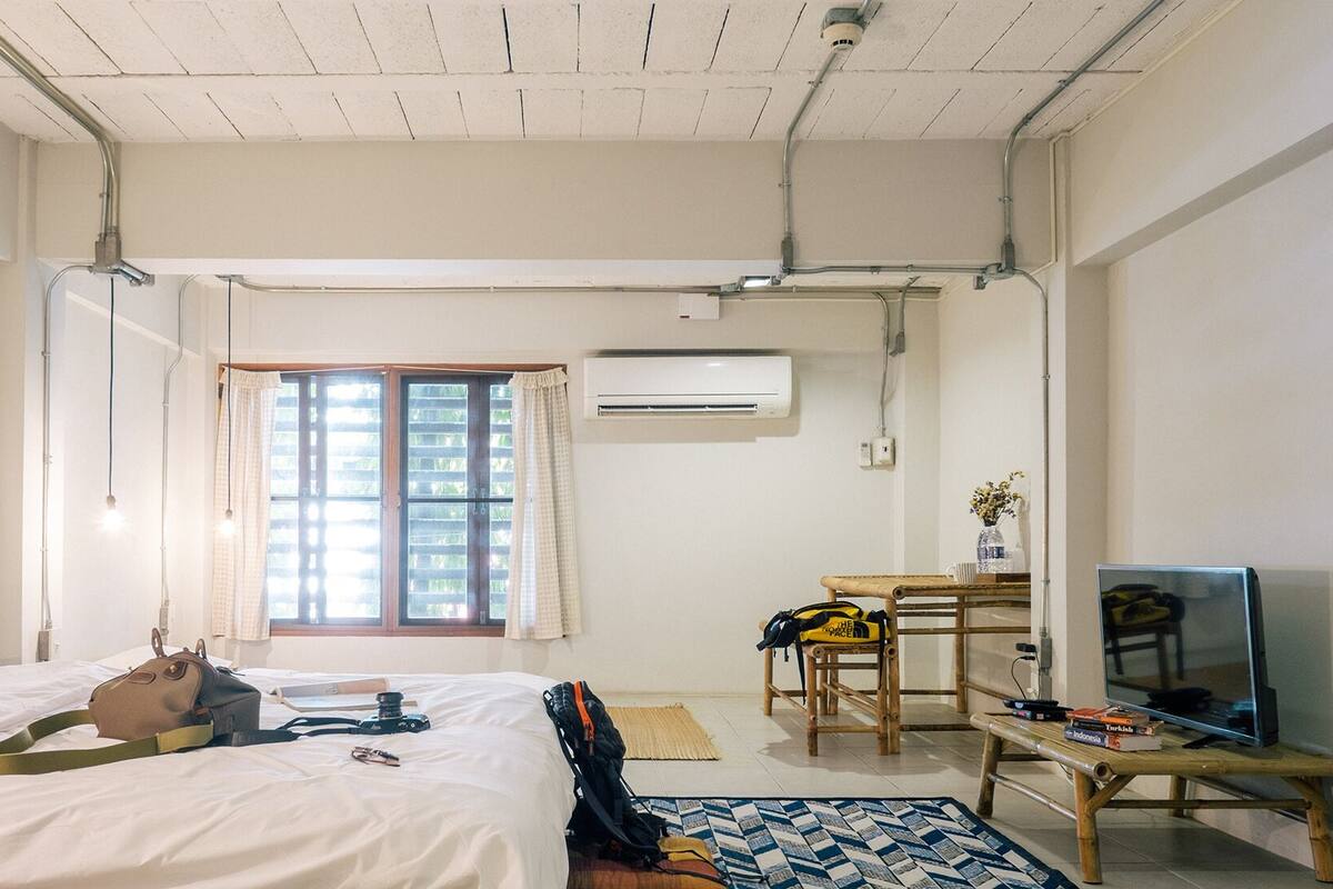 A hotel room with a bed, a desk with a chair, a television, and an air conditioning unit.