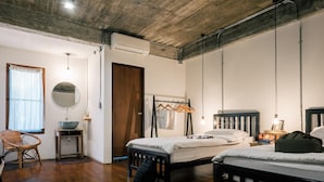 A bedroom with a wooden floor, a bed, a bedside table with a bowl, a hanging light, a wardrobe, and a window with a curtain. - Happynest Inspiring Hostel (Chiang Rai)