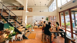 A spacious cafe with high ceilings, wooden floors, and large windows. - Happynest Inspiring Hostel (Chiang Rai)
