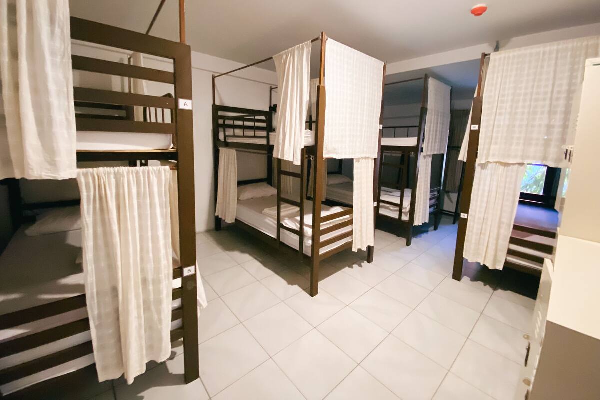 A dormitory room with bunk beds, white curtains, and a television in the corner.