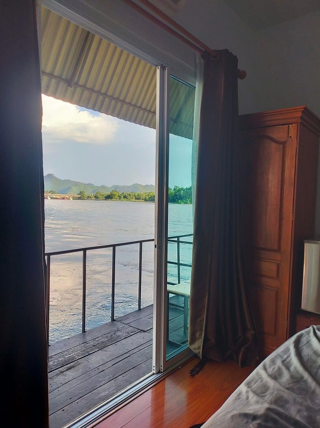 A room with a sliding glass door leading to a balcony overlooking a body of water and distant mountains.