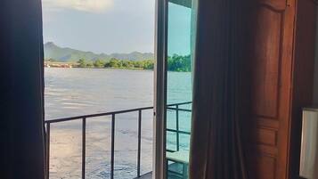 A room with a sliding glass door leading to a balcony overlooking a body of water and distant mountains.