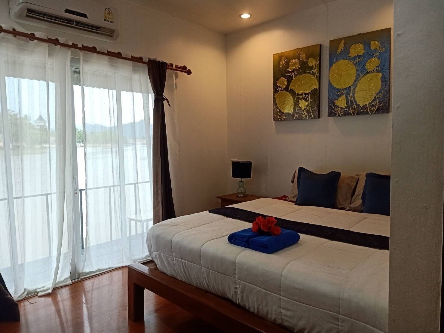 Una habitación de hotel con cama, mesita de noche, lámpara y cuadros en la pared.