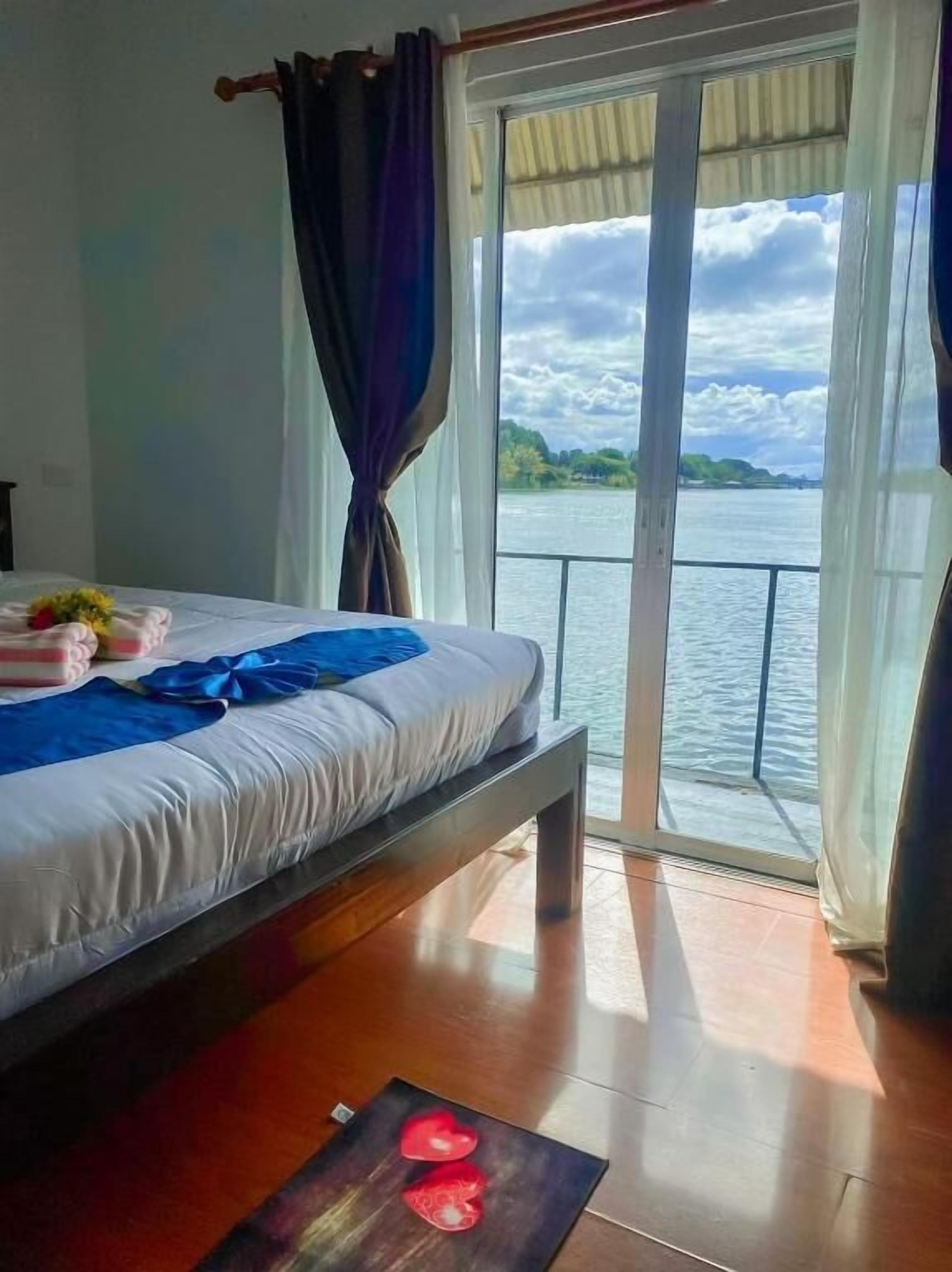 Ein Schlafzimmer mit einem Bett, Blick auf ein Gewässer durch eine Glastür und Holzboden.