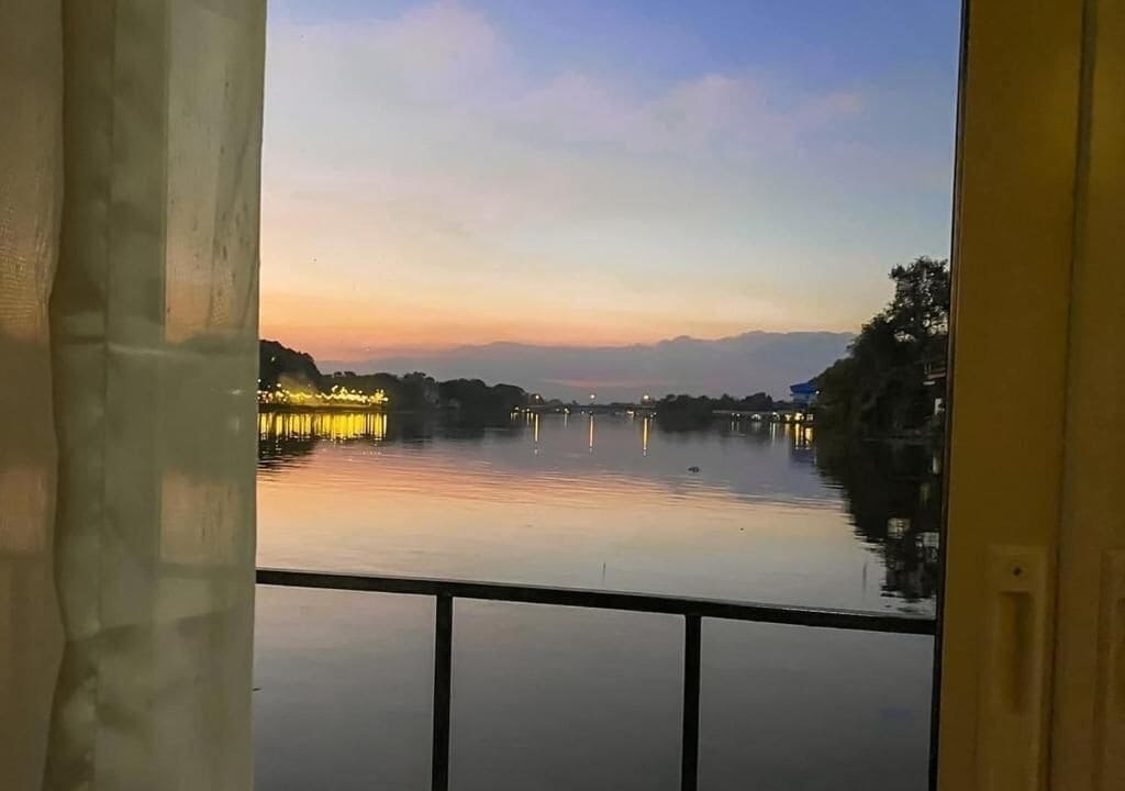 Vista de uma varanda com vista para um corpo d'água calmo, uma ponte e montanhas ao longe.