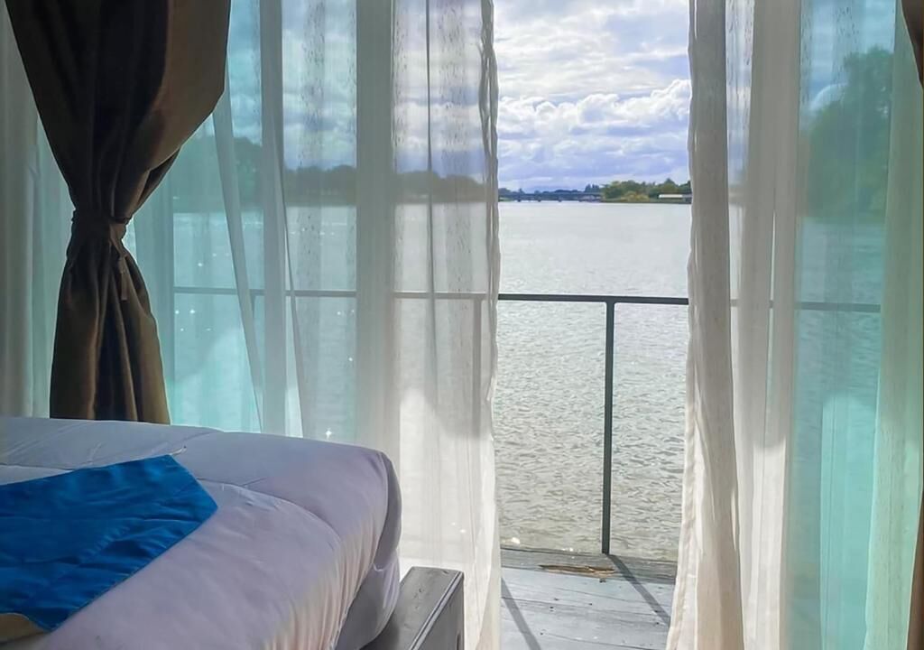 A room with a bed, a view of a body of water, and a balcony with a railing.