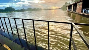 A river with a wooden structure on the right bank, a metal railing in the foreground, and a partly cloudy sky. - Tara Raft Kanchanaburi (Kanchanaburi)