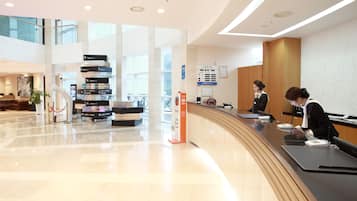 Un moderno vestíbulo de hotel con un mostrador de recepción curvo, un directorio digital y una escalera que sube a un nivel superior.