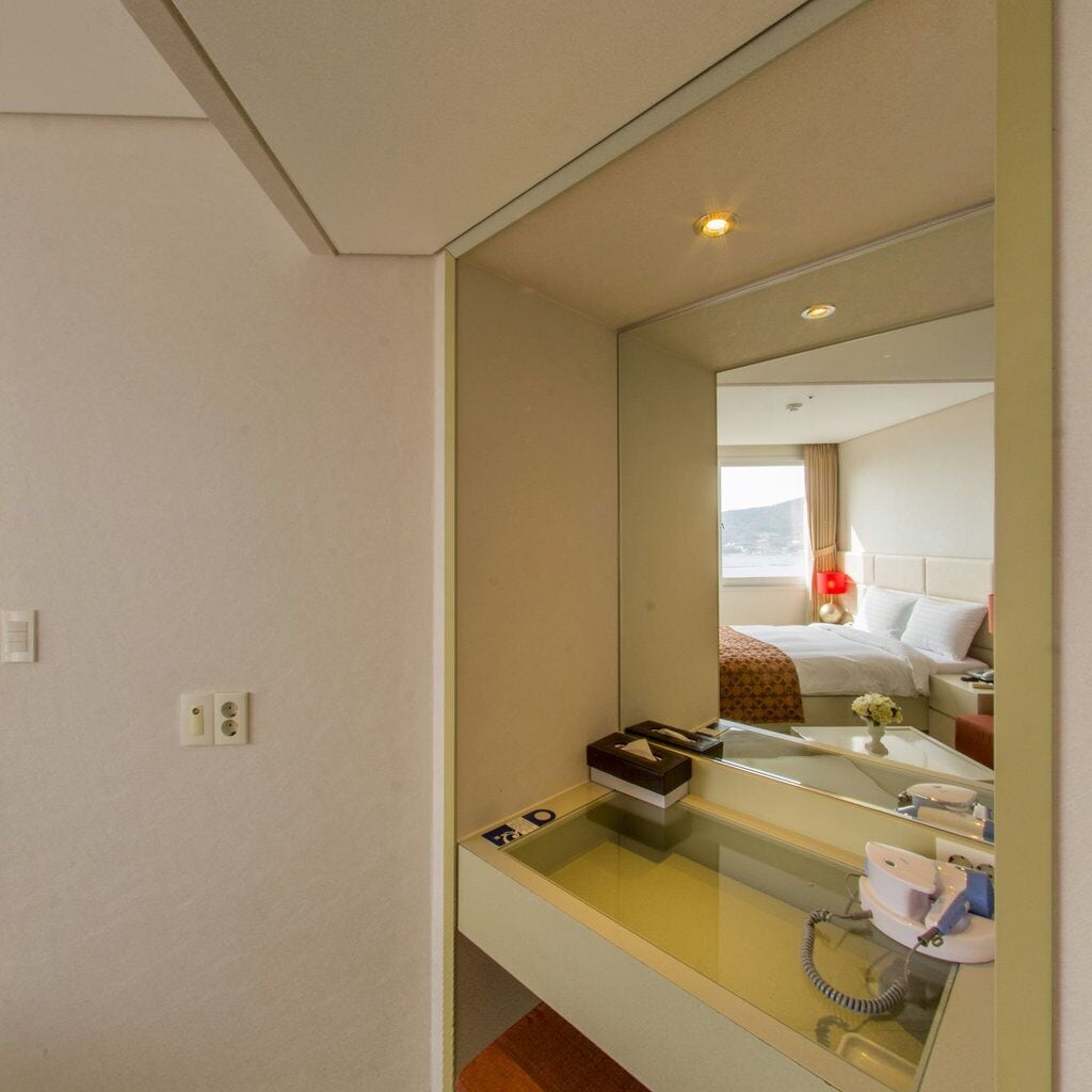 Une chambre d’hôtel dotée d’un grand miroir, d’une table de chevet avec un téléphone et d’une fenêtre donnant sur l’extérieur.