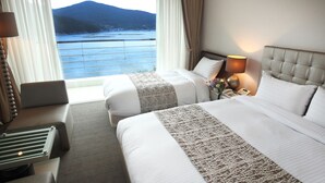 A hotel room with two beds, a desk, a lamp, and a view of a body of water and mountains.