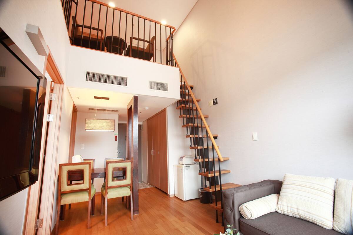 A compact living space with a dining area, a sofa, a staircase, and a small kitchen area.