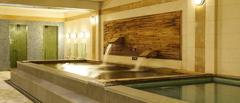 A spa area with a hot tub, a wooden wall panel, and a tiled wall with a green mosaic.