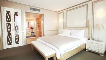 A hotel room with a large bed, a bedside table with a lamp, a bench, a wardrobe, and a mirror.