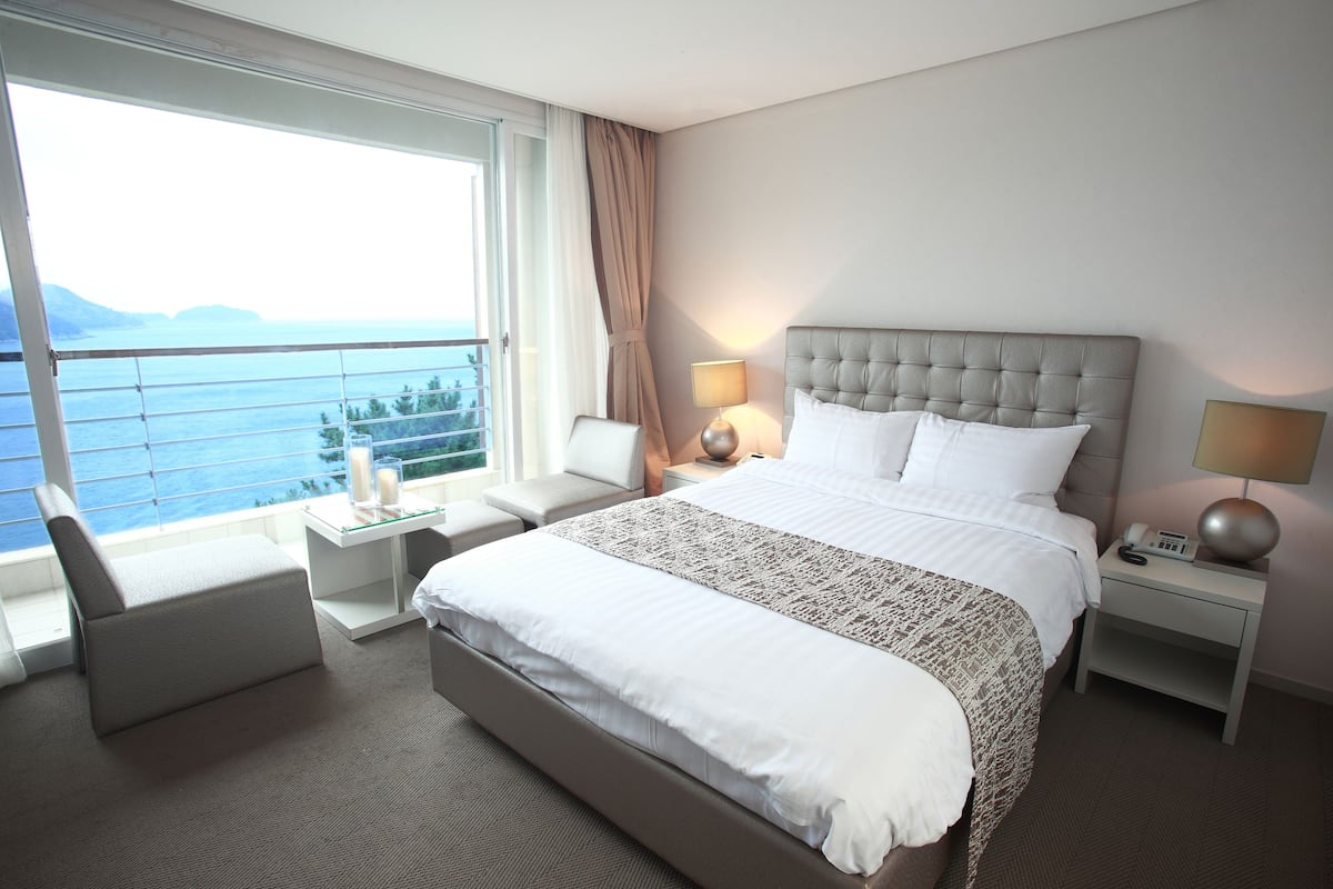 A hotel room with a large bed, a desk, a chair, and a view of the sea.