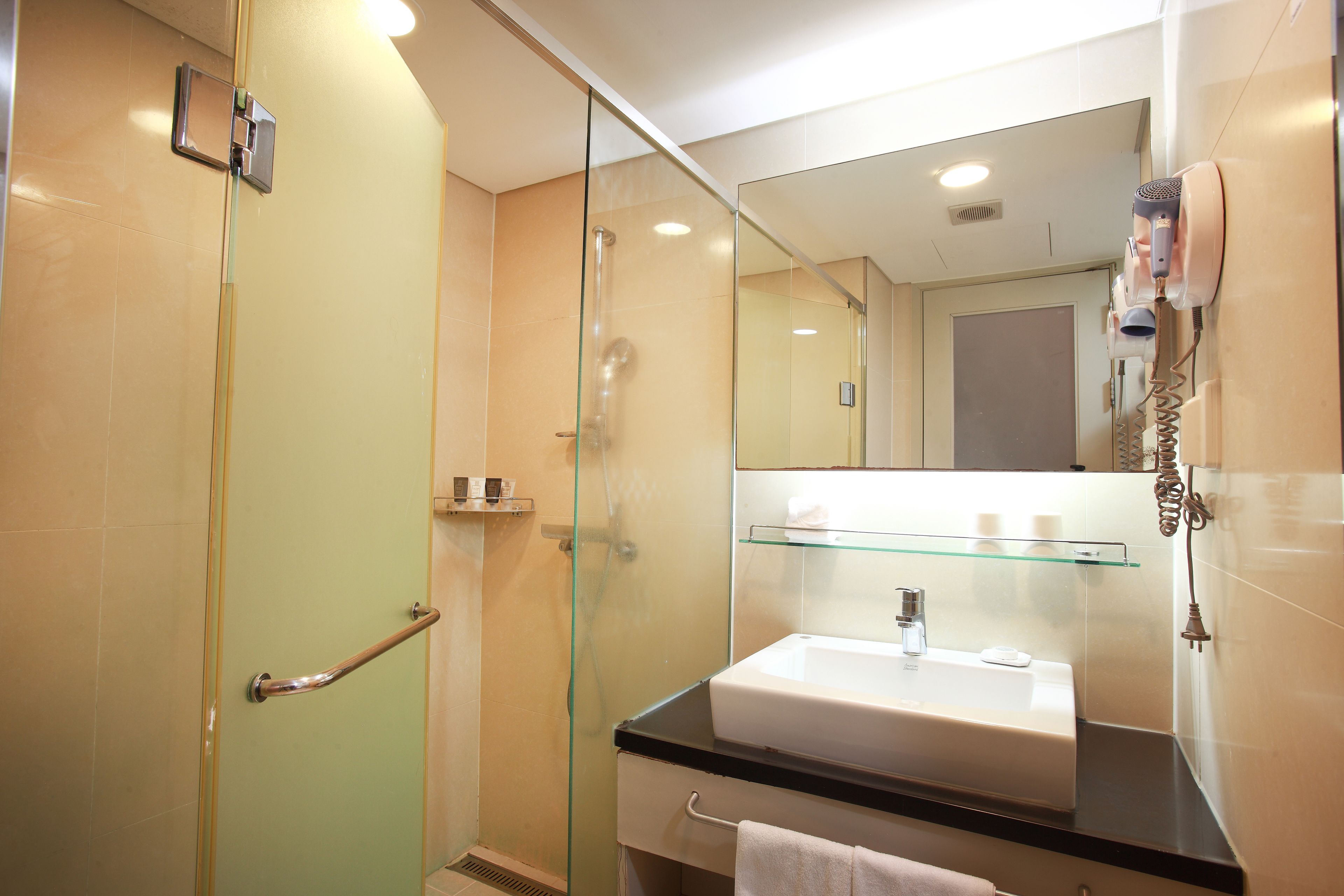 Un baño moderno con cabina de ducha de vidrio, un lavabo blanco y un espejo con secador de pelo montado en la pared.