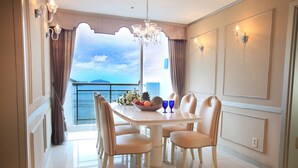 A dining area with a table and chairs, a chandelier, and a view of the sea through a large window.