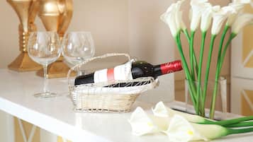 A bottle of wine in a basket on a counter, two empty wine glasses, and a bouquet of white flowers.