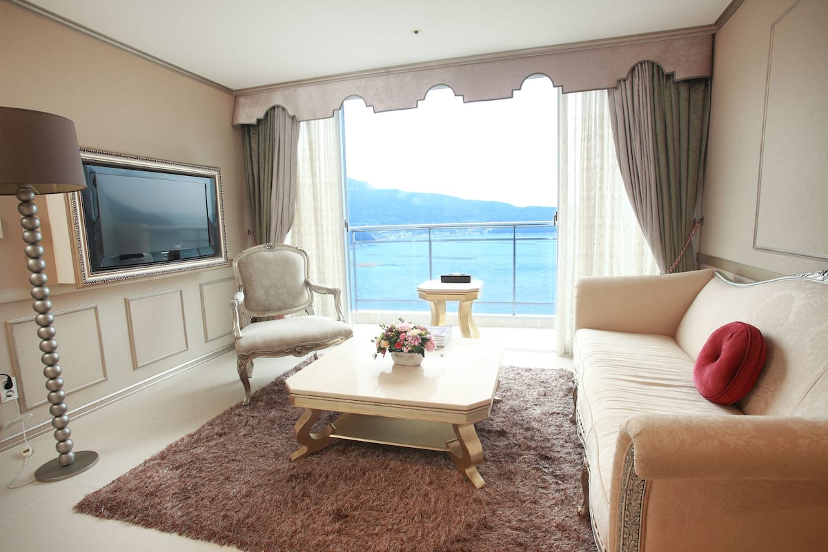 A living room with a sofa, a coffee table, a TV, and a view of the sea.