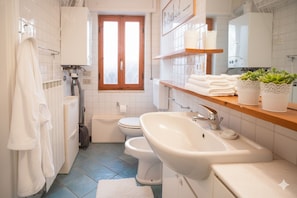 A modern bathroom with a toilet, bidet, sink, and a window. - Appartamento Profumo di Mare (Cipressa)